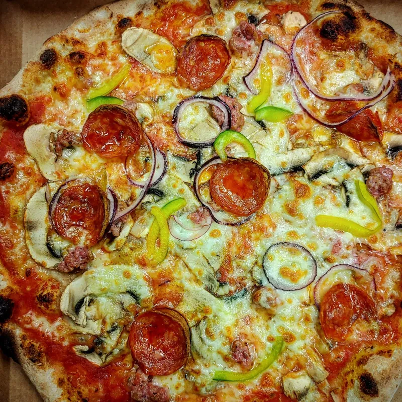 Pizza tonda con salame piccante, salsiccia, funghi, cipolla rossa e peperoni